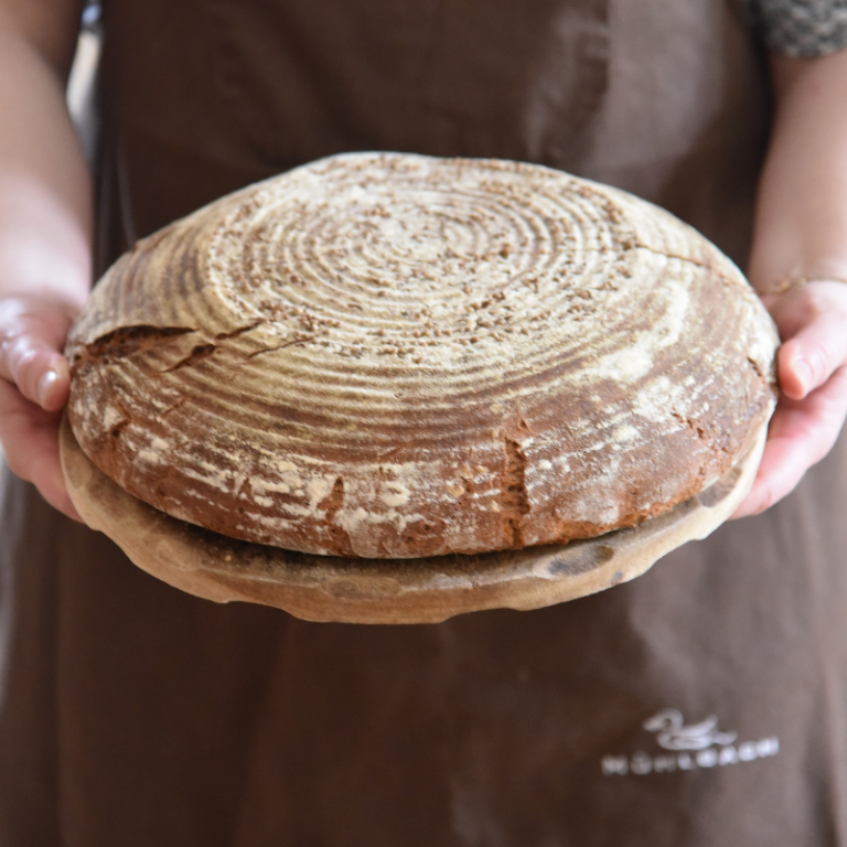 Ein rundes Sauerteigbrot wird auf einem Holzbrett serviert