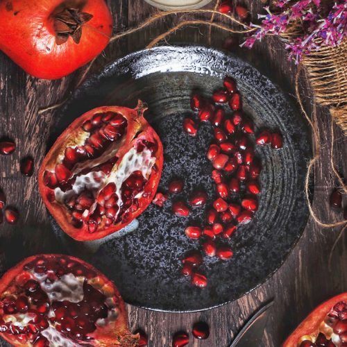 Aufgeschnittener Granatapfel mit Granatapfelkernen auf einem schwarzen Teller