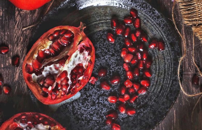 Aufgeschnittener Granatapfel mit Granatapfelkernen auf einem schwarzen Teller